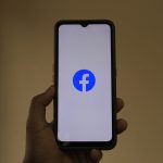 Mão segurando um smartphone com o logotipo do Facebook na tela.