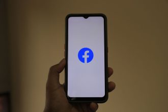 Mão segurando um smartphone com o logotipo do Facebook na tela.