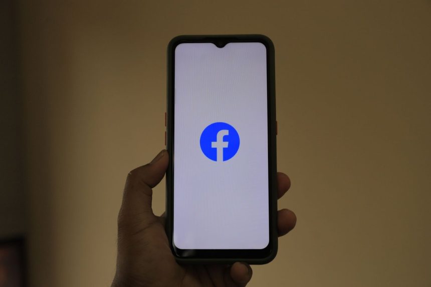 Mão segurando um smartphone com o logotipo do Facebook na tela.