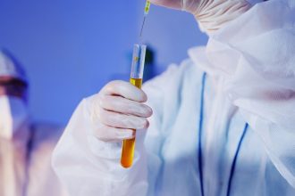 Cientista usando equipamentos de proteção realiza um teste com um tubo em um laboratório.