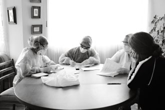 Profissionais de saúde usando equipamentos de proteção participam de uma reunião em torno de uma mesa.