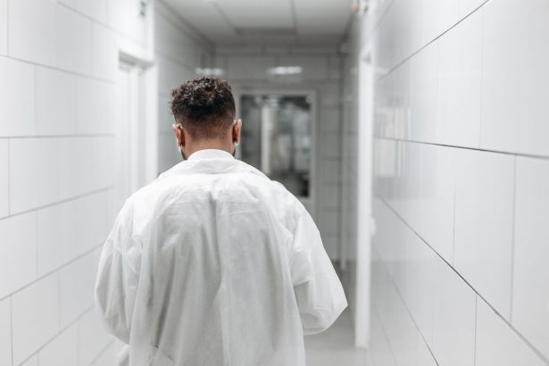 Profissional de saúde de jaleco caminha por um corredor iluminado de hospital, visto de costas.