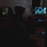 Profissional analisa dados em múltiplos monitores em uma sala escura de operações de cibersegurança.