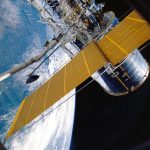 Espaçonave com painéis solares orbitando a Terra, vista contra o espaço.